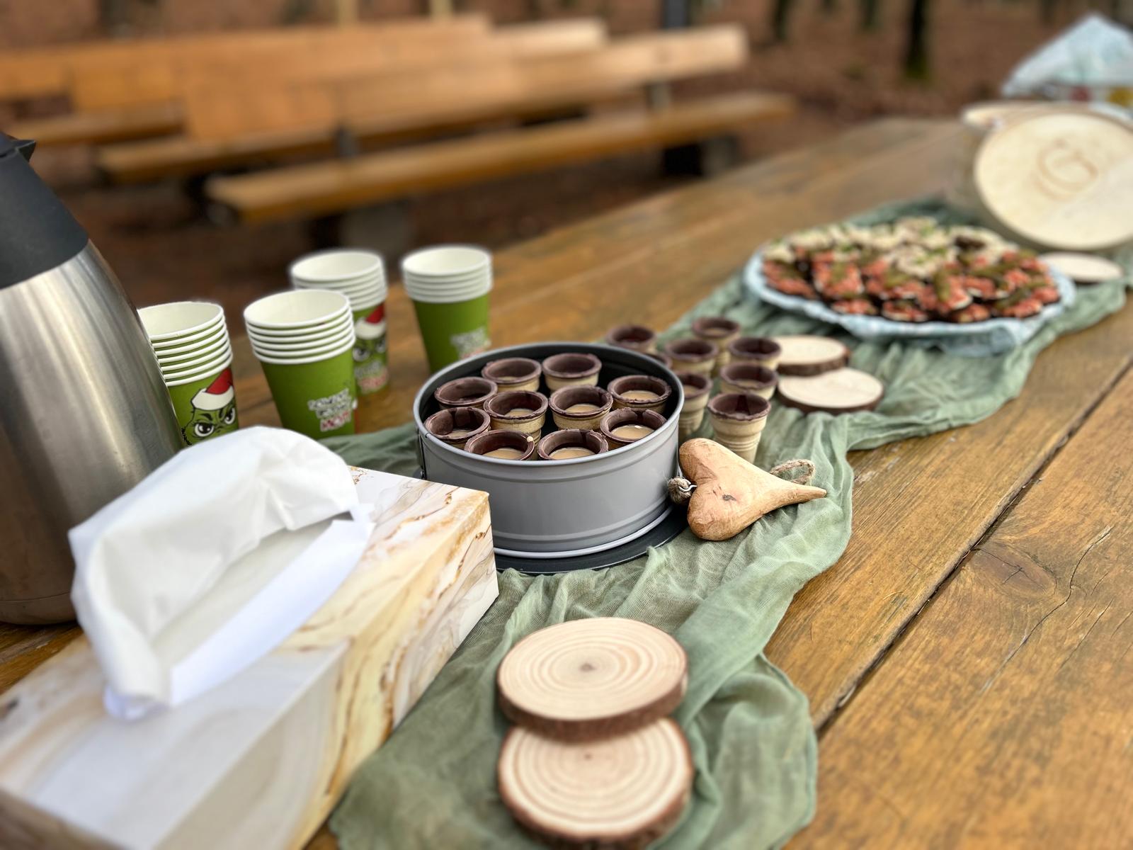 Festlich gedeckter Holztisch mit Kaffee, herzhaften Häppchen und süßen Kleinigkeiten bei einer Feier im Wald
